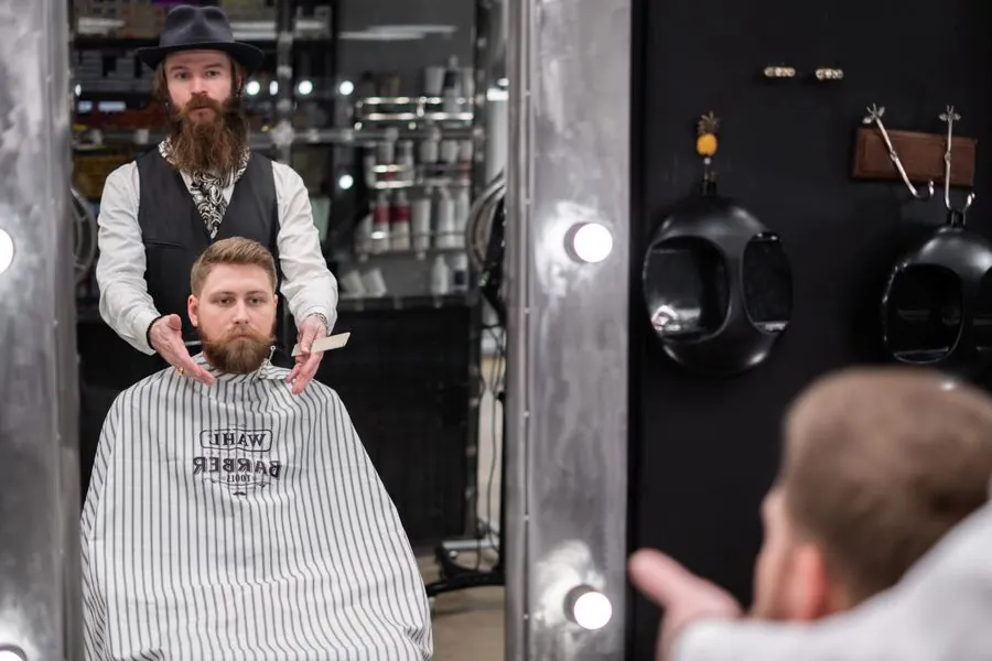 A barber standing behind a seated customer in a cape