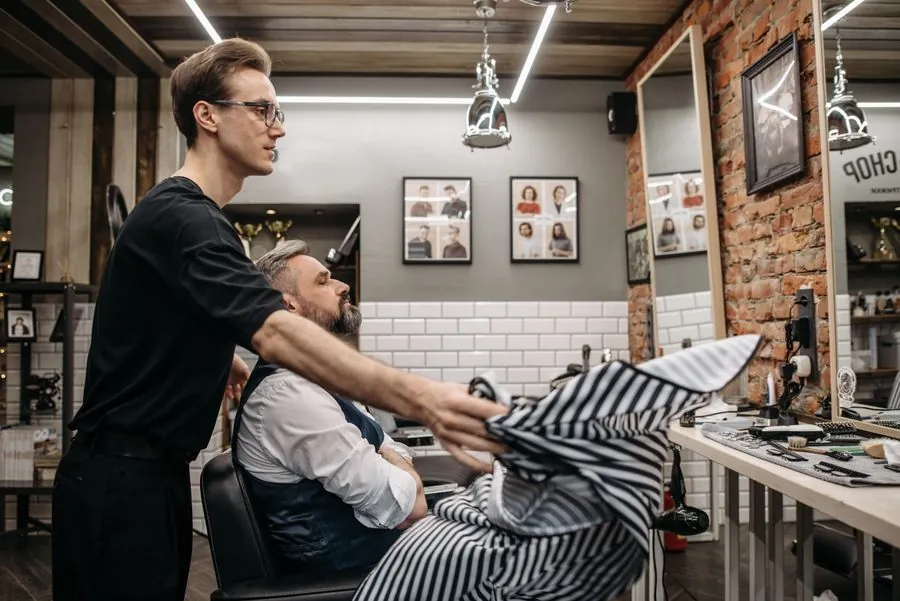 A barber shaving a customer under bright shop lights