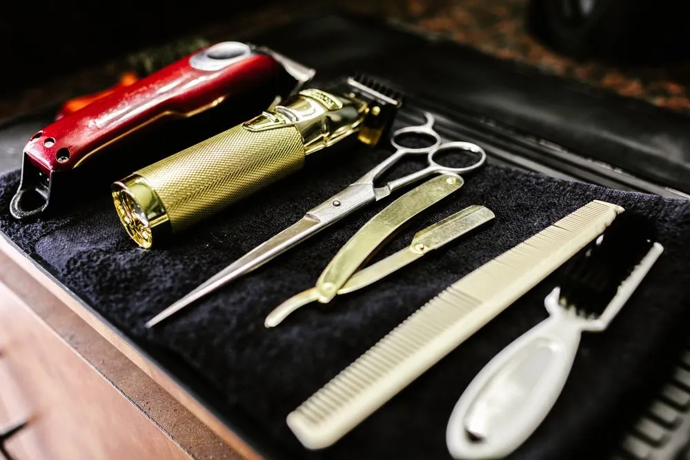Clippers, scissors and a razor laid out on a black cloth