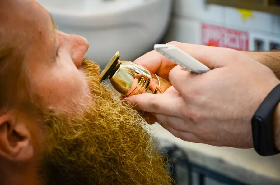 A close view of a barber trimming a red beard